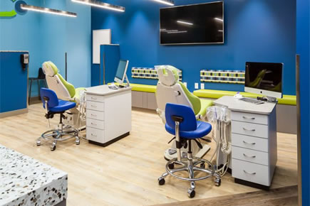 Modern orthodontic office with blue walls, dental chairs, and treatment stations equipped with monitors.