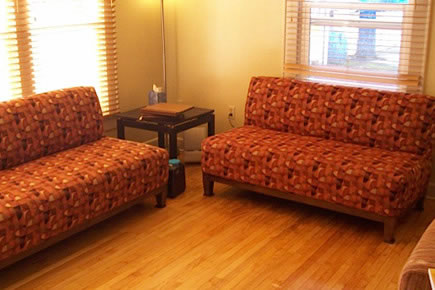 Waiting room with two orange patterned couches, wooden floor, and side table.