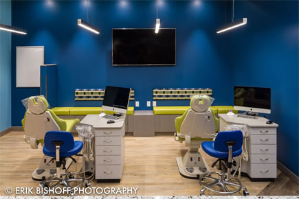 Modern orthodontic office with two treatment stations, blue walls, and dental equipment setup.